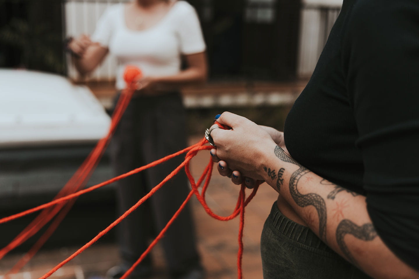 Dos personas tejiendo una red con cuerdas rojas en la calle